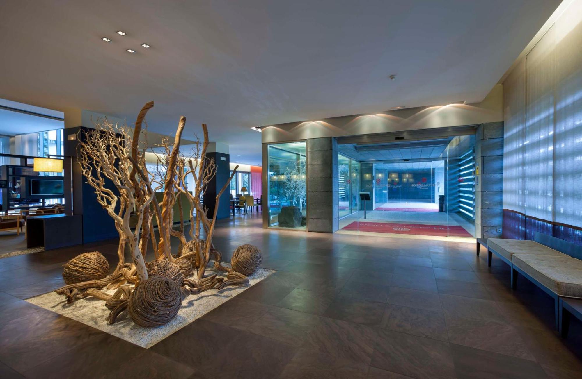 Nh Collection Santiago De Compostela Hotel Exterior photo The photo shows a modern lobby interior design. In the center, there is an artistic installation featuring natural materials, including twisted branches and round formations, possibly representing organic elements. The flooring is made of large tiles