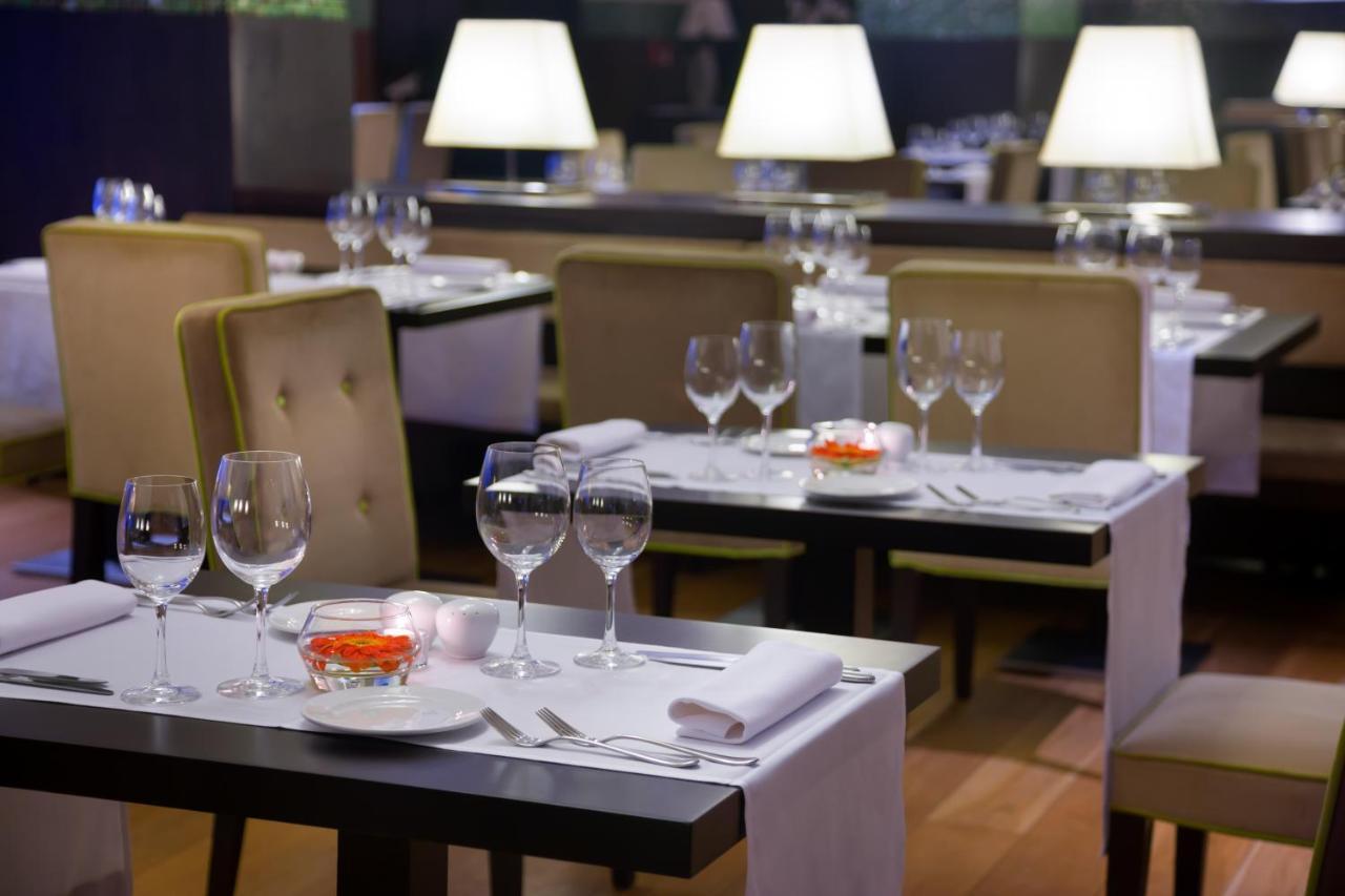 Nh Collection Santiago De Compostela Hotel Exterior photo The photo shows a restaurant interior featuring several tables arranged with elegant settings. Each table is equipped with white tablecloths, plates, and various glassware, including wine glasses. Small decorative items are placed at the center of th