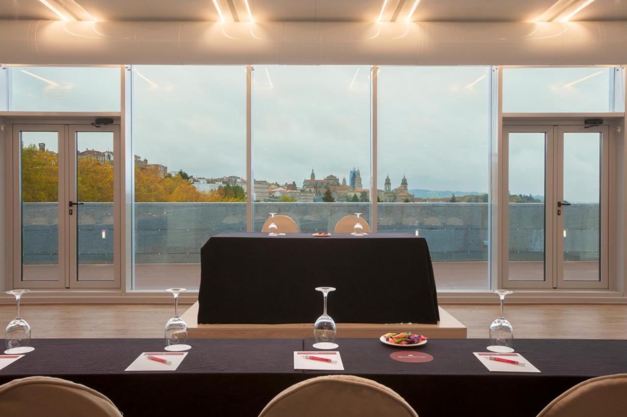 Nh Collection Santiago De Compostela Hotel Exterior photo The photo shows a modern conference or meeting room featuring a long table set with plates and glasses. In the foreground, a black tablecloth covers the central table, and there's a small dish of food positioned on it. The setting has large windows t