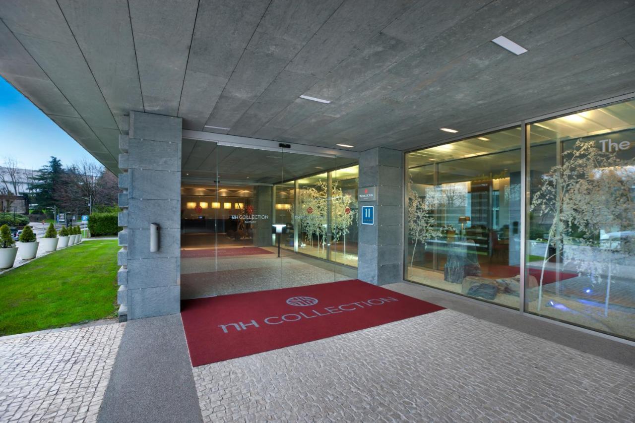 Nh Collection Santiago De Compostela Hotel Exterior photo The photo shows the entrance of a modern hotel, specifically the TH Collection. The building features a sleek design with a concrete facade and large glass windows. A red welcome mat with the hotel’s logo is placed at the entrance. The surrounding ar