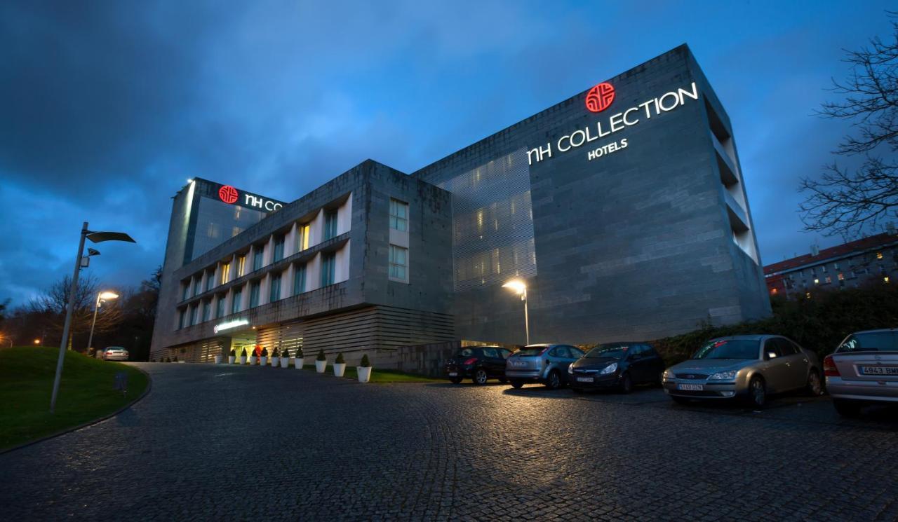 Nh Collection Santiago De Compostela Hotel Exterior photo The photo shows a modern hotel building, identified as "NH COLLECTION HOTELS," with a sleek, contemporary design. The structure is illuminated in the evening light, highlighting its architectural features. The entrance area has a few cars parked, and
