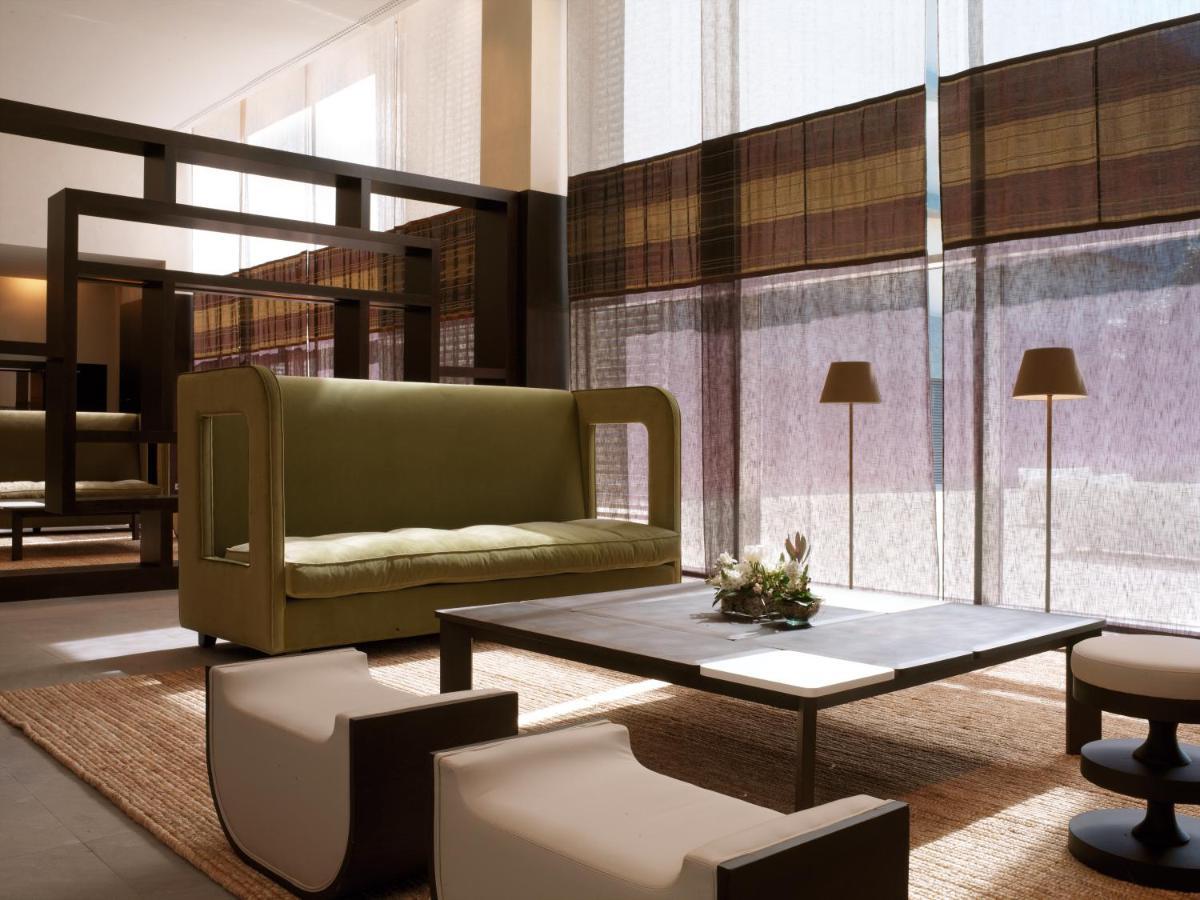 Nh Collection Santiago De Compostela Hotel Interior photo The photo depicts a modern and stylish living space. It features a green sofa with distinctive armrests, paired with a simple coffee table at the center. There are two contemporary chairs, one white and one dark, positioned around the table. The floo